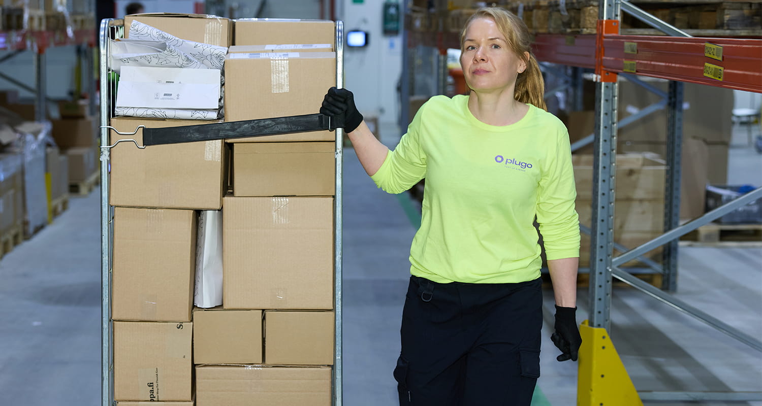Warehouse worker pulling a roll cage loaded with orders down a warehouse aisle